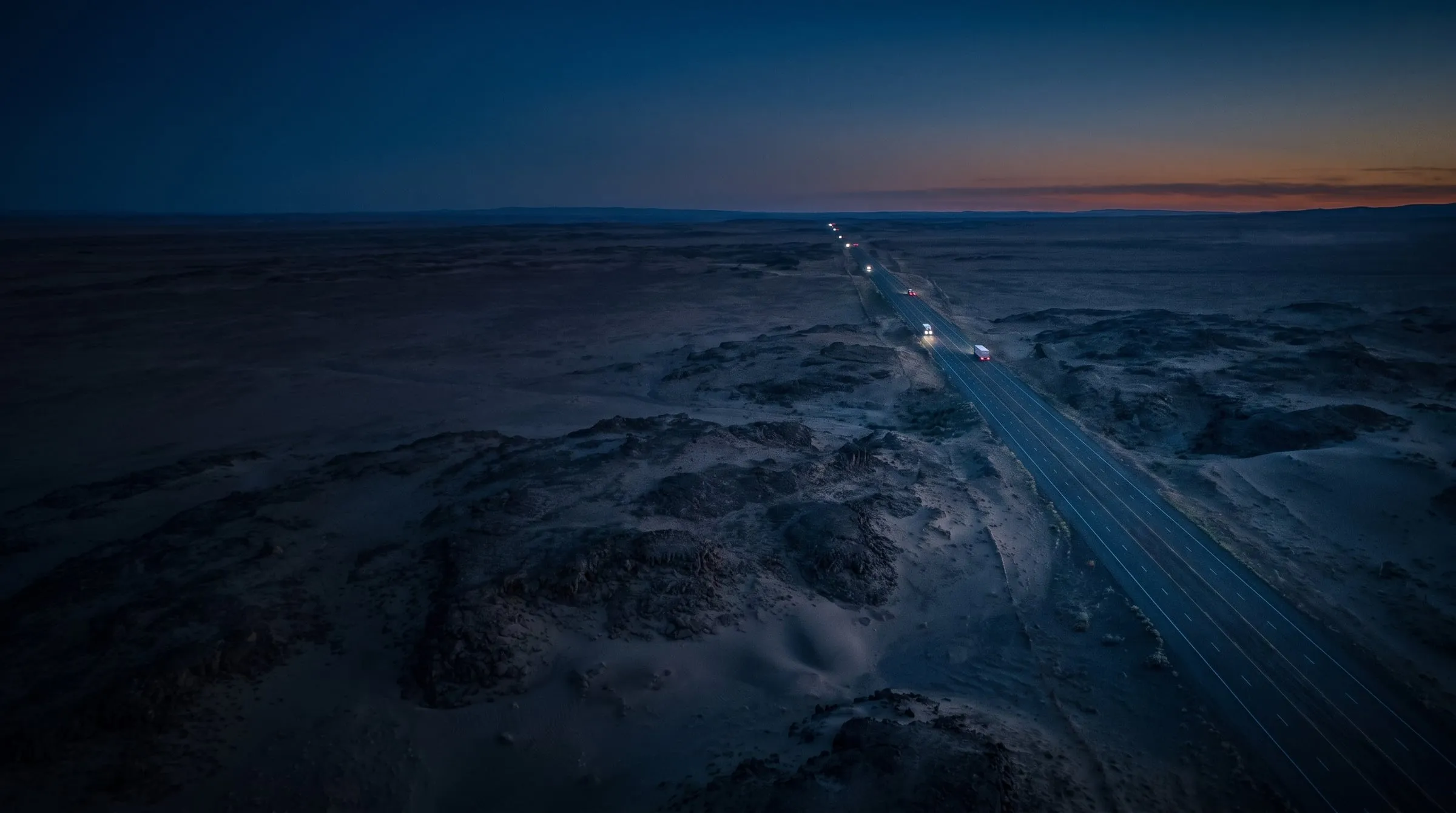 An aerial view of trucks on a desert highway at dusk.